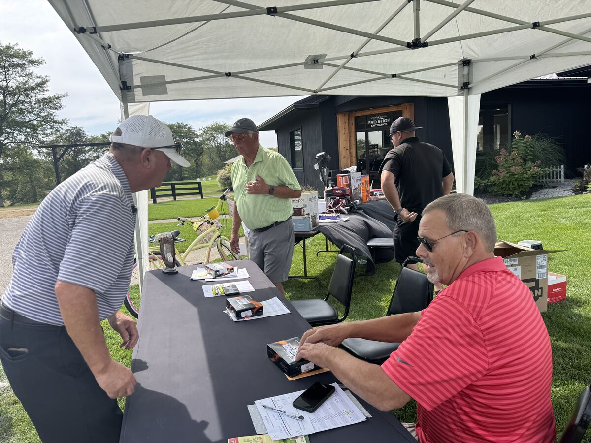 Volunteers running the check-in table under a tent beside the pro shop, with raffle prizes displayed behind them